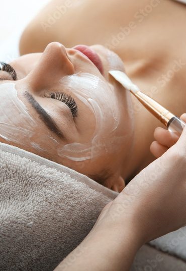 Cosmetologist applying mask on client's face in spa salon